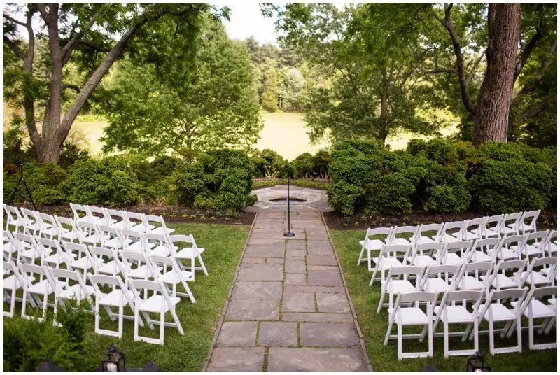 White folding chairs on both sides of a stone path leading to a garden ceremony spot