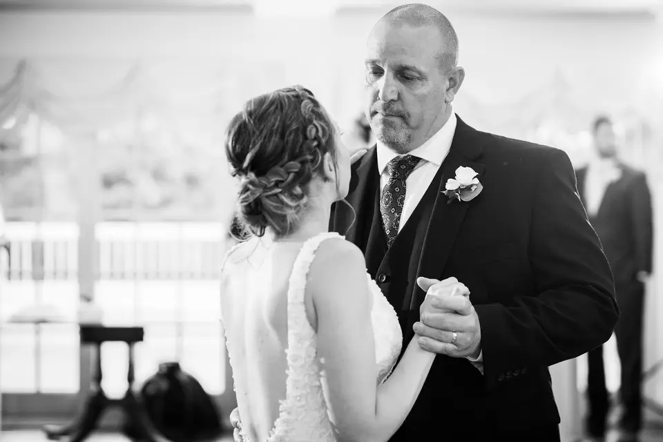 Black and white photo of a bride dancing with her father in a bright reception room