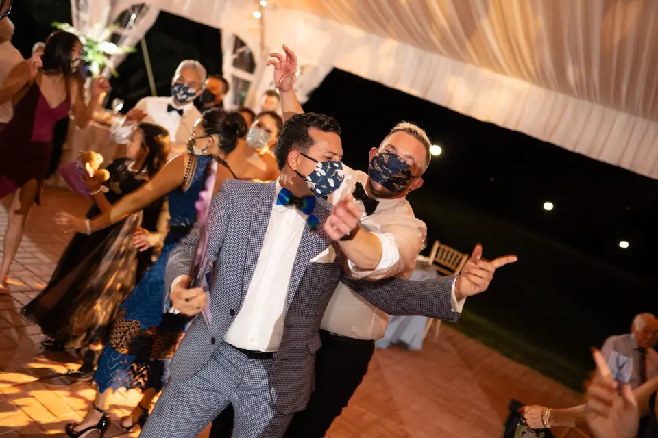 Guests in face masks dancing and posing on a brick reception floor at night under a tent