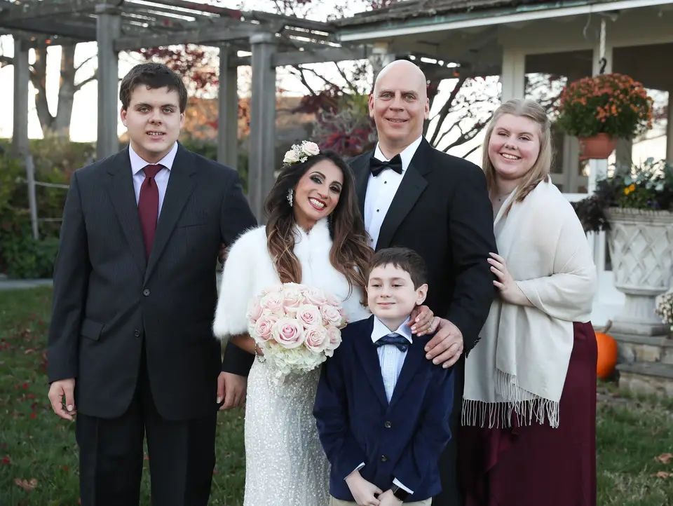 Bride and groom pose with two boys and a young woman outside on a fall day