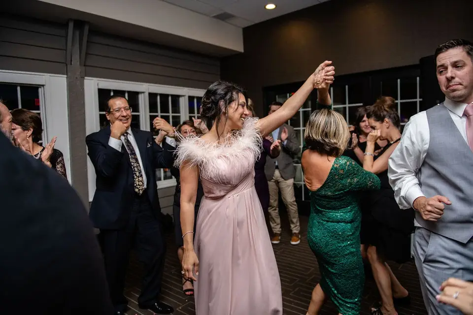 Woman in a pink feathered dress dancing with her arm raised among reception guests