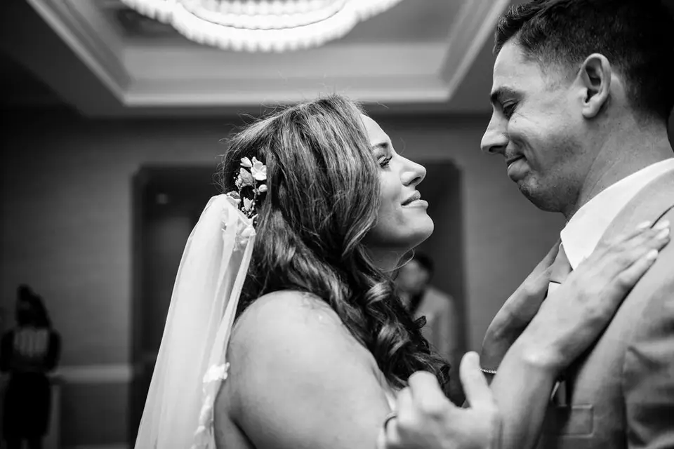Black and white photo of a bride in a floral hair piece and veil gazing at the groom during a dance