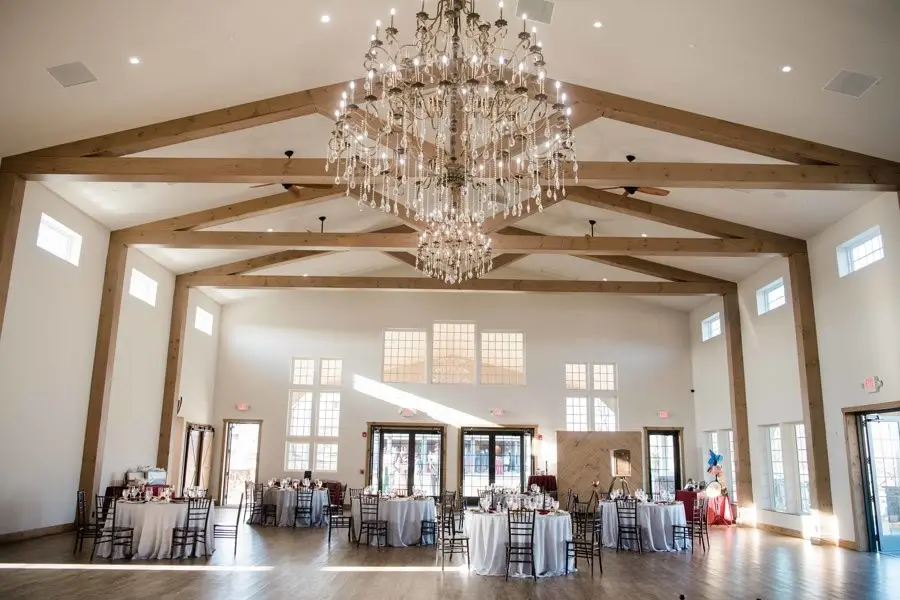 Empty reception hall with a large chandelier, exposed wood beams and round tables set for guests