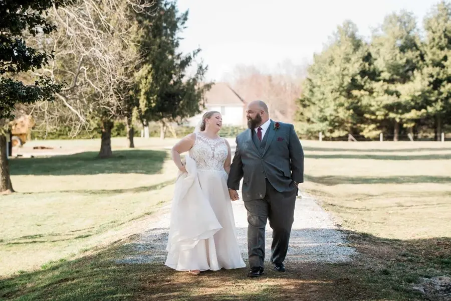 Bride and groom walking hand in hand down a gravel path through a grassy field