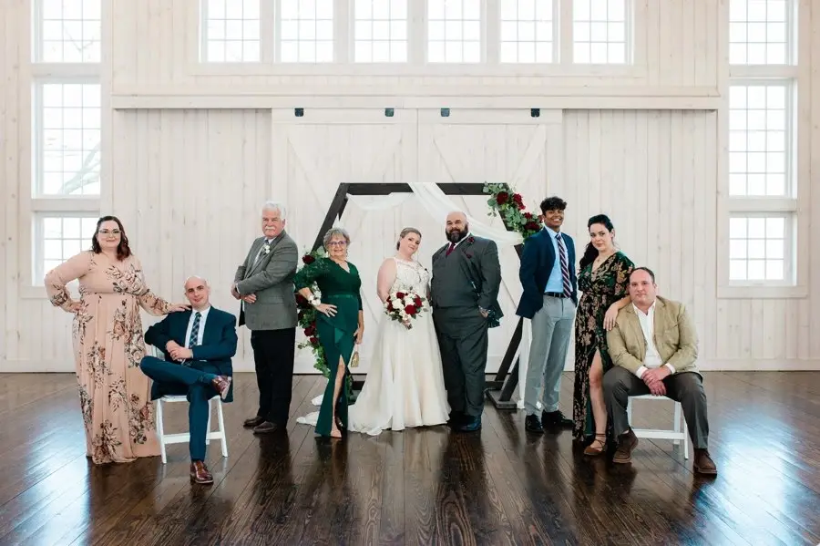 Bride and groom with seven family members posed in front of the ceremony arch in a white barn venue
