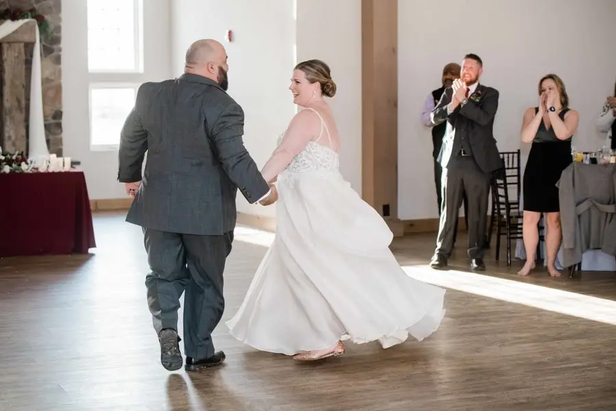 Bride and groom dancing their first dance on a wood floor as guests clap