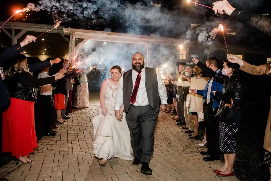 Bride and groom walking through a sparkler send-off as guests line a brick path at night