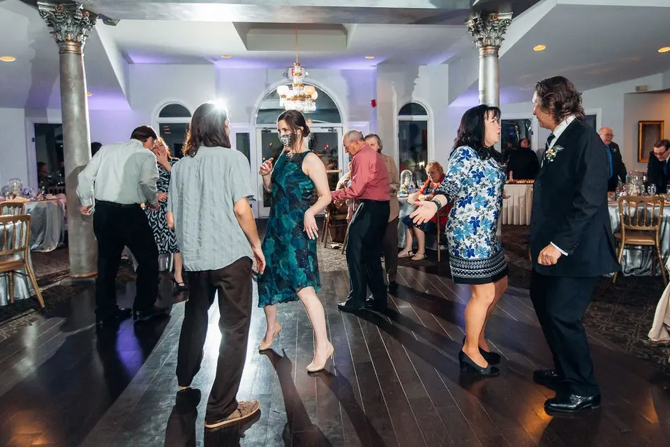 Guests dancing on a dark wood dance floor in a venue with white columns and arched windows