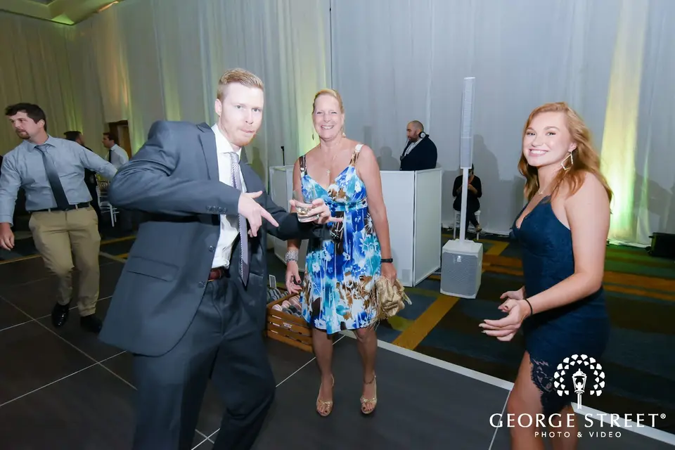 Man pointing and dancing with two women on a hotel ballroom dance floor near the DJ setup