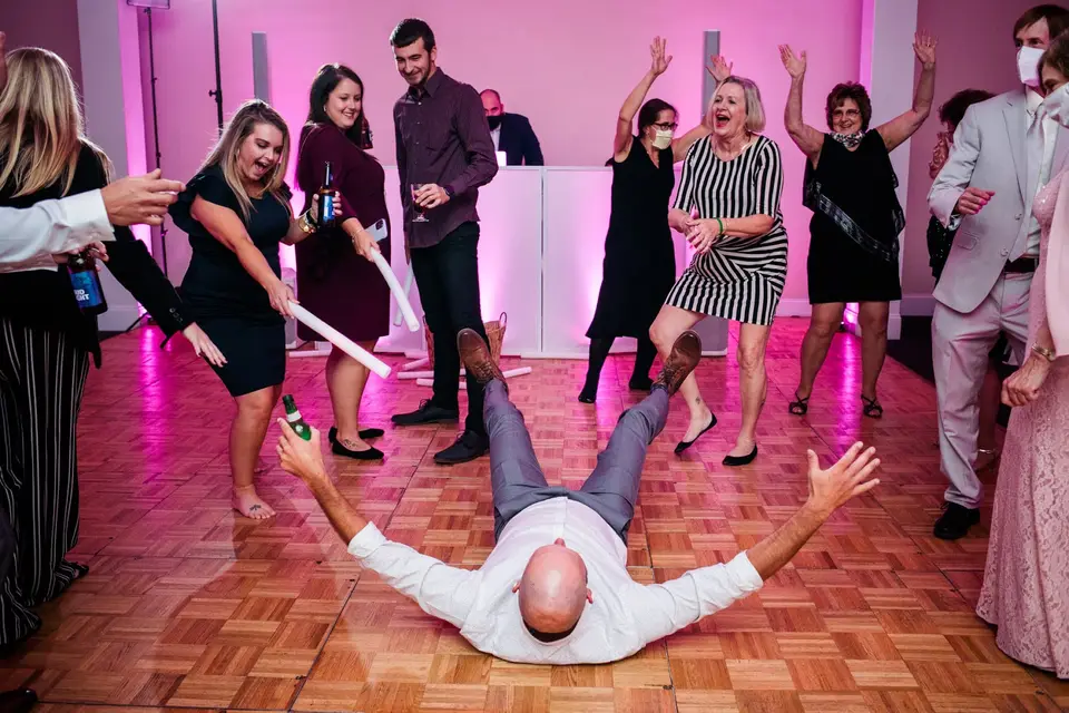 Guest lies on his back on a parquet dance floor while others dance and cheer under pink lighting