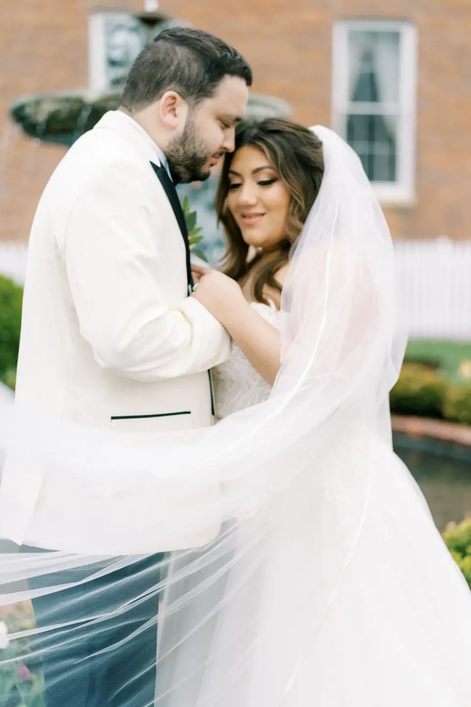 Close-up of a groom in a white dinner jacket holding the bride, her sheer veil blowing around them
