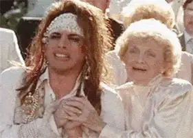 Man with long hair and a headband looking distressed next to an older woman in a movie still
