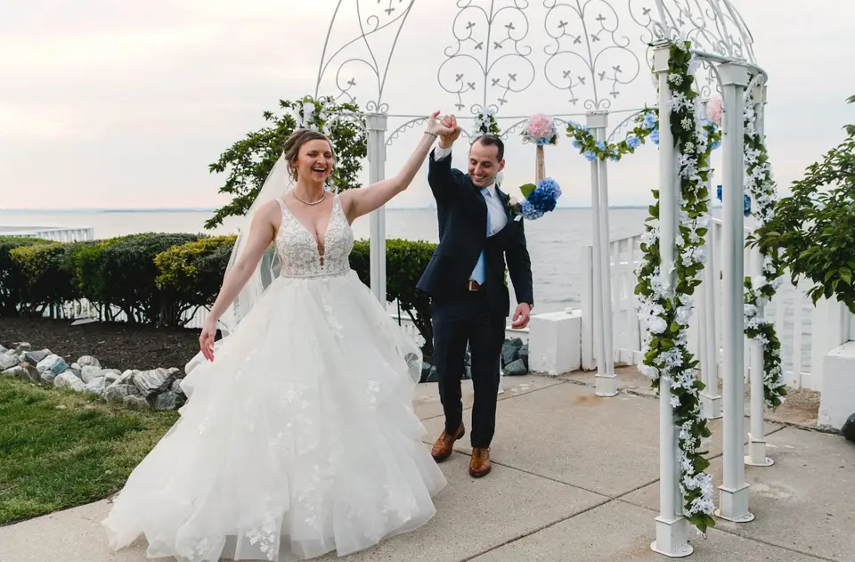 Bride and groom raising joined hands and laughing beside the floral gazebo after their ceremony