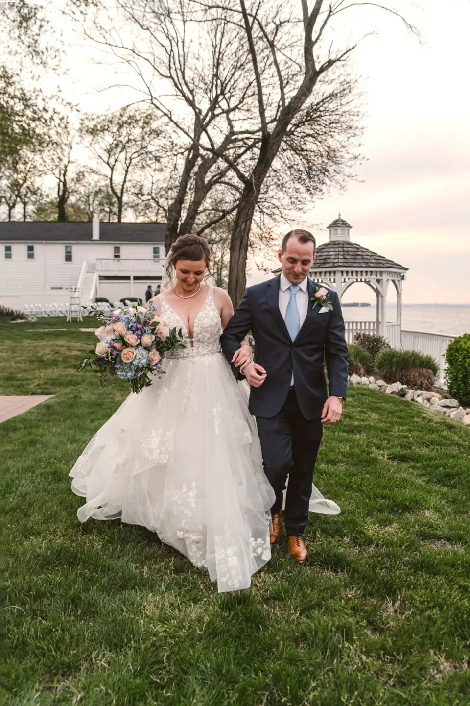 Allayne and Stephen walking arm in arm across a lawn with a white house and waterfront gazebo behind them