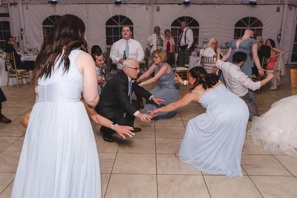 Guests in light blue dresses and suits dancing and bending low on the tent dance floor at a wedding