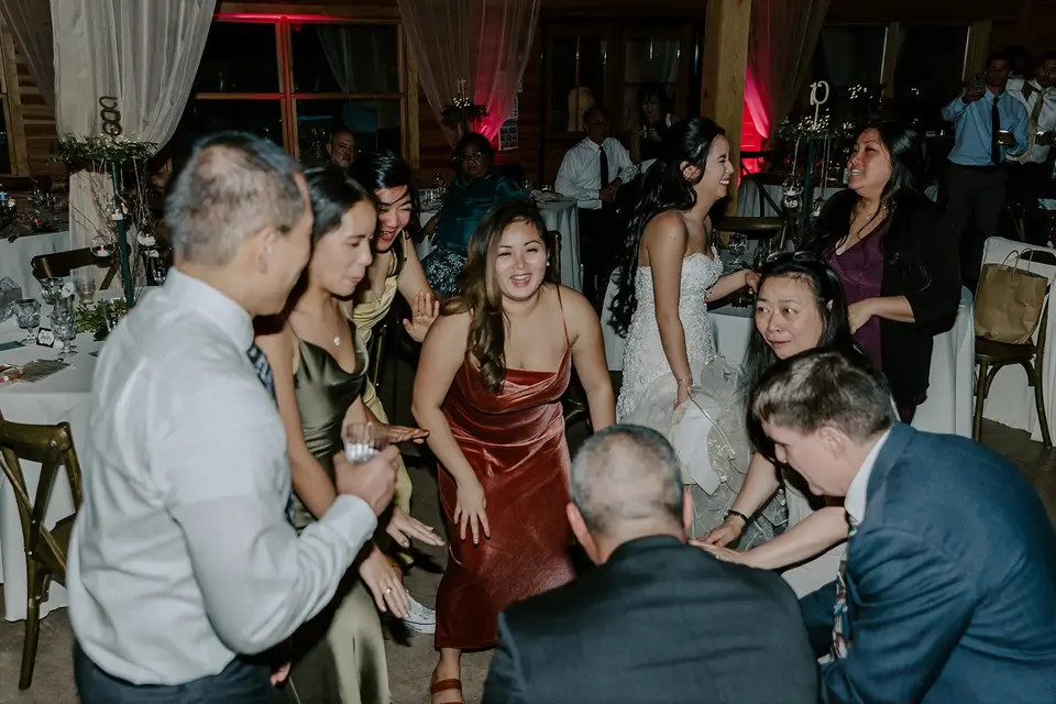 Wedding guests dancing and laughing on a dance floor in a barn-style venue with red uplighting
