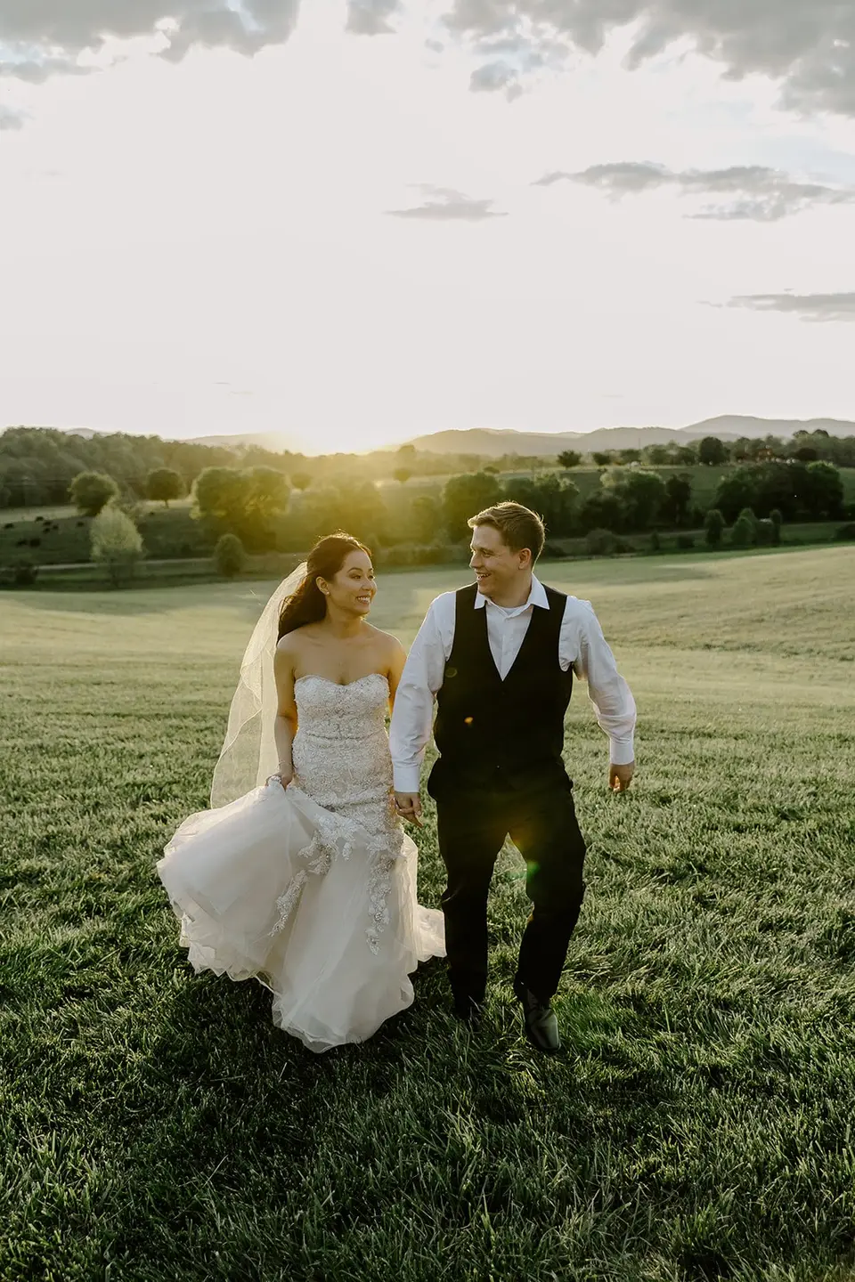Bride and groom walking hand in hand across a grassy field at sunset