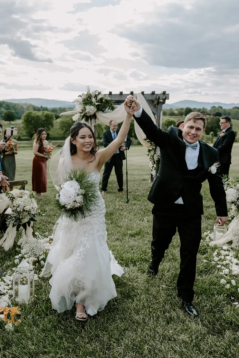 Bride and groom raising joined hands as they walk back up the aisle after an outdoor ceremony