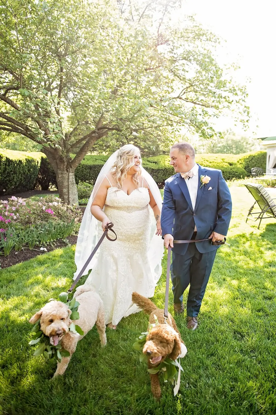 Bride and groom walking on the lawn with two goldendoodles wearing leaf garlands