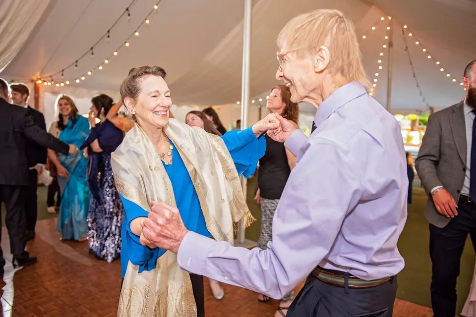 Older couple dancing hand in hand on the parquet dance floor under a string-lit tent