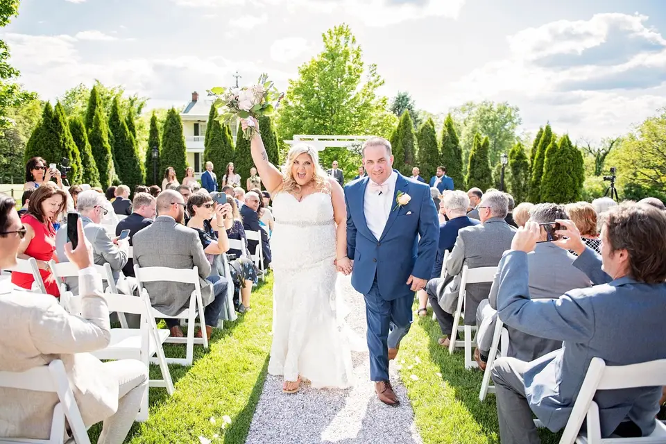 Newlyweds walk hand in hand up the outdoor aisle past seated guests after the ceremony