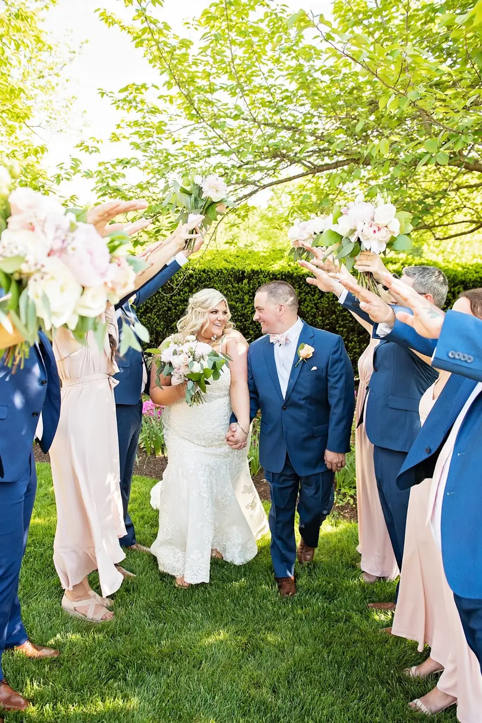 Bride and groom walk through an arch of wedding party members holding up flowers