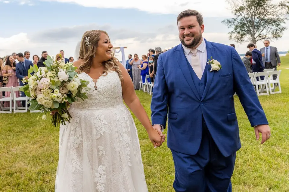 Smiling bride and groom holding hands as they walk down the grass aisle after their ceremony