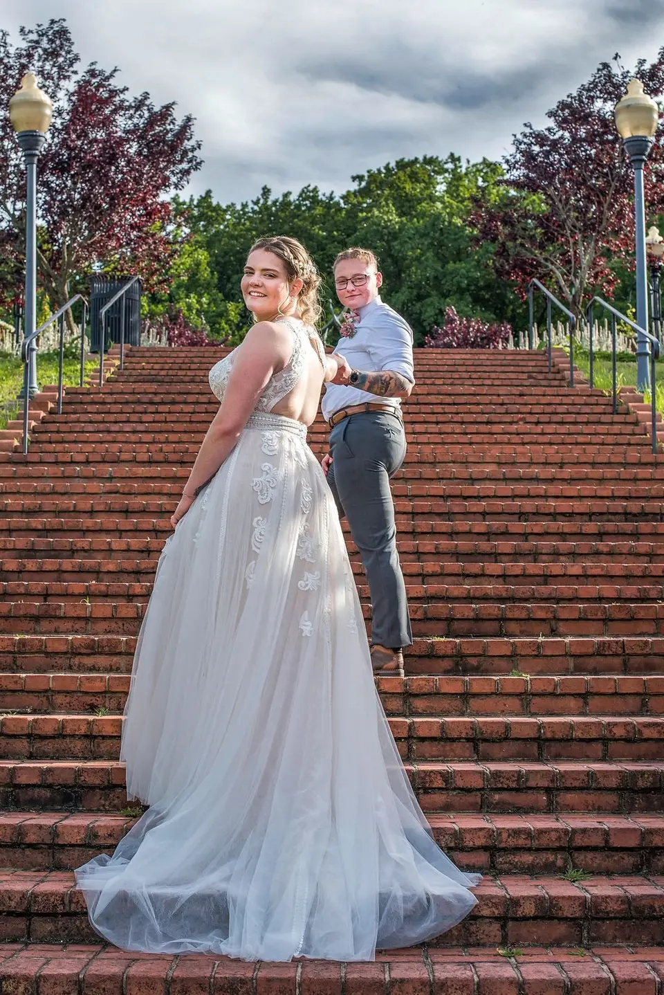 Bride in a tulle gown looks back over her shoulder while holding her partner's hand on a wide brick staircase