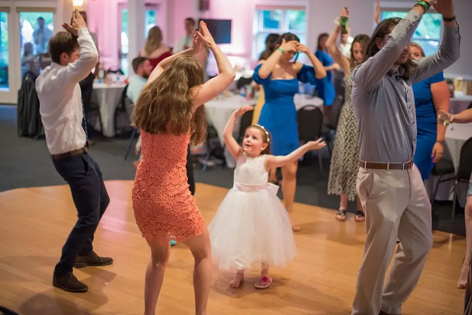 Guests and a little girl in a white tutu dress dance together on a wooden dance floor
