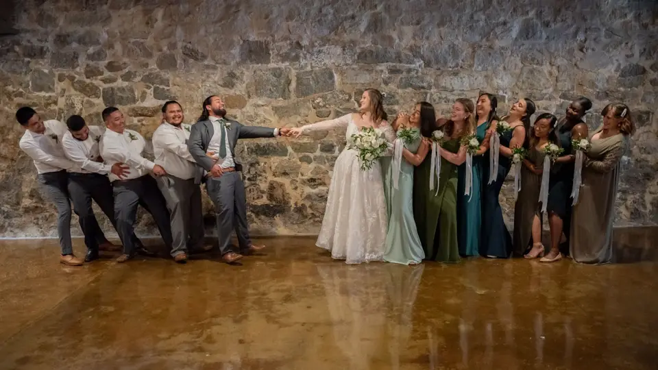 Groomsmen playing tug of war with the bride and bridesmaids across a stone-walled room