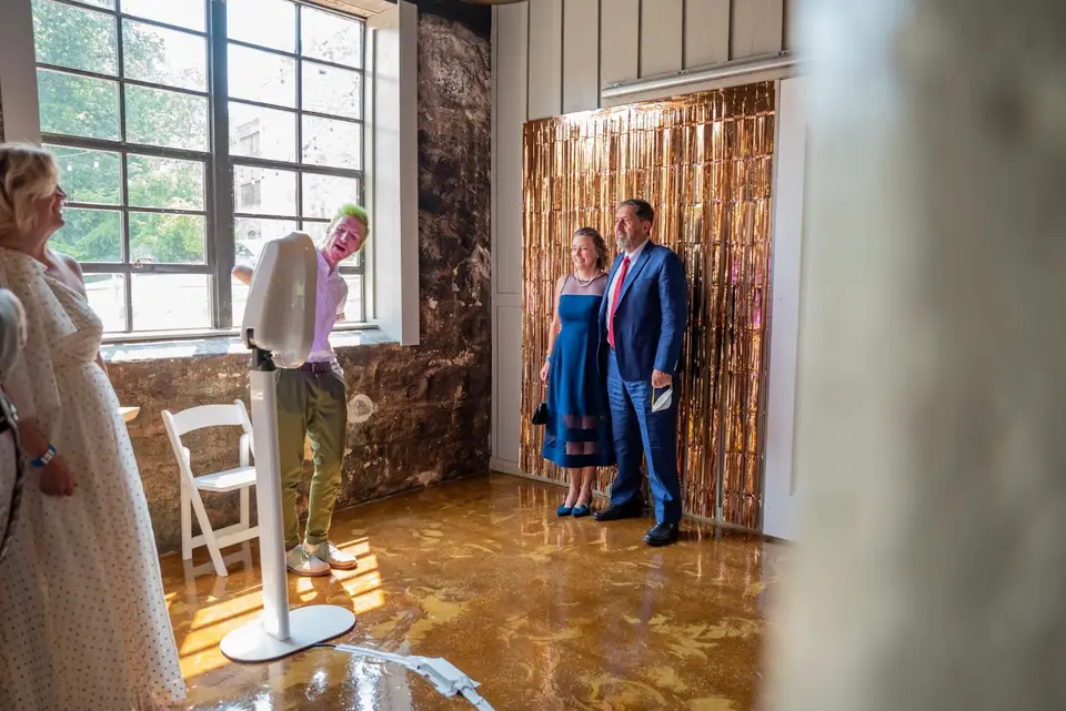 Guests posing in front of a gold fringe backdrop while a man operates a white photo booth kiosk