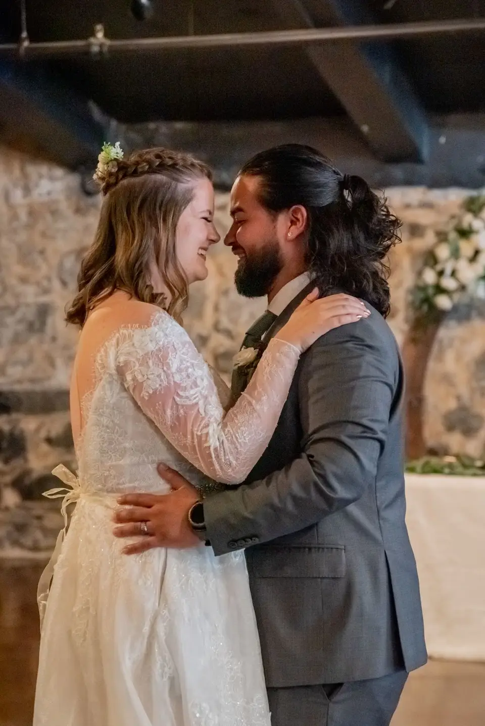 Bride and groom touching foreheads and smiling during their first dance in a stone-walled venue