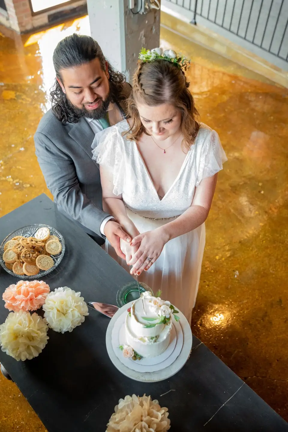 Bride and groom cutting a small wedding cake on a dark table, seen from above