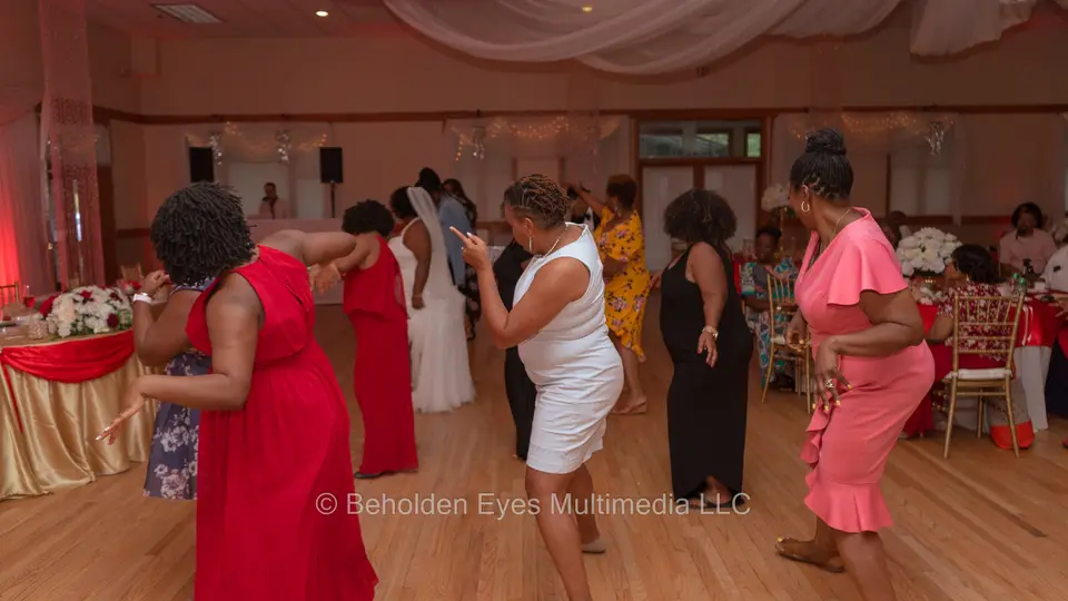 Women in red, pink and black dresses dancing at a reception with the bride in the background