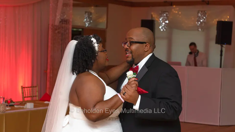 Bride and groom dancing close together in a red-lit reception room with the DJ booth behind