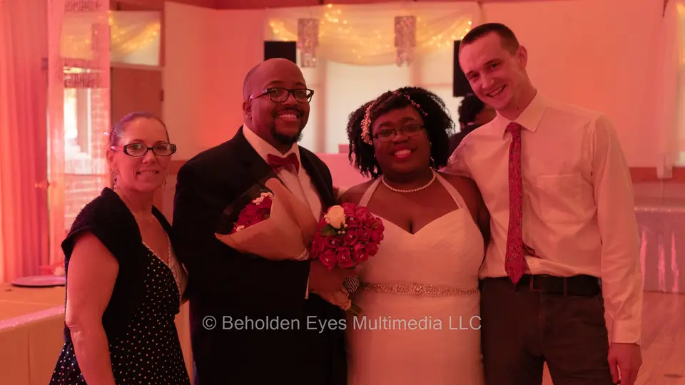 Bride and groom with two guests posing for a photo under warm red reception lighting