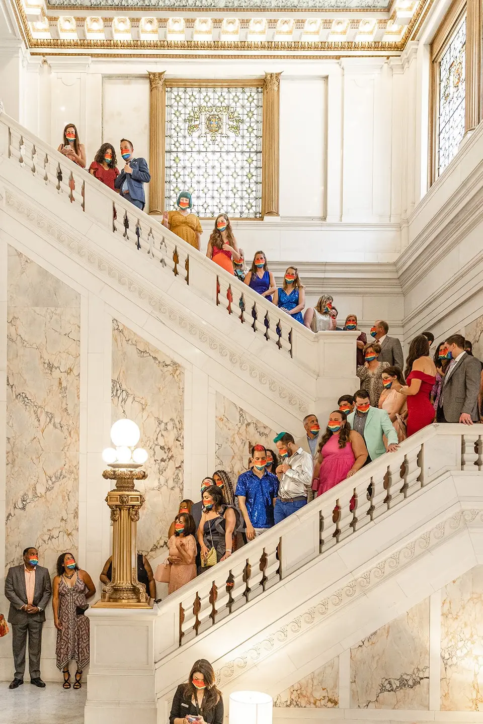 Wedding guests in masks lining a marble staircase in a grand building