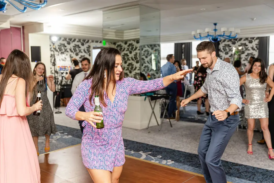 Woman holding a green bottle and dancing with a man at a hotel ballroom reception