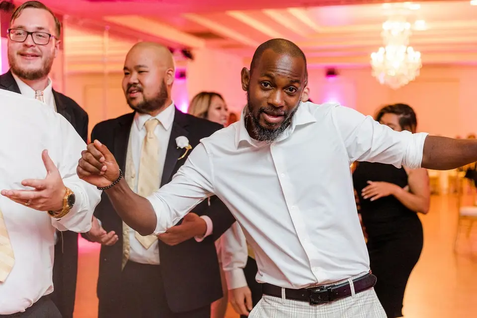 Guest in a white shirt dancing with an animated expression among other guests under pink lighting