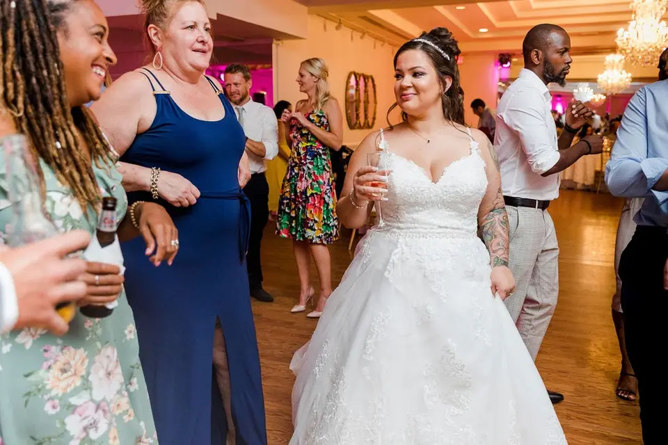 Bride in a white gown smiling at guests on the dance floor at a pink-lit reception