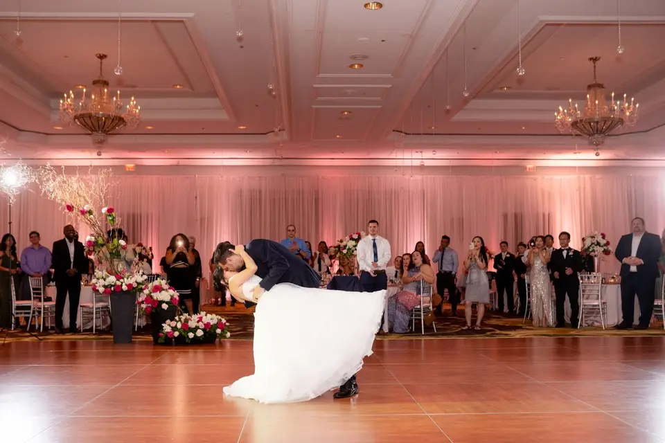 Groom dipping bride during their first dance on a ballroom dance floor as guests watch