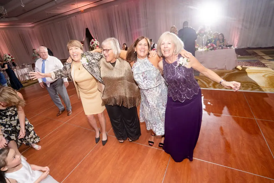 Four women linked arm in arm dancing together on a ballroom dance floor