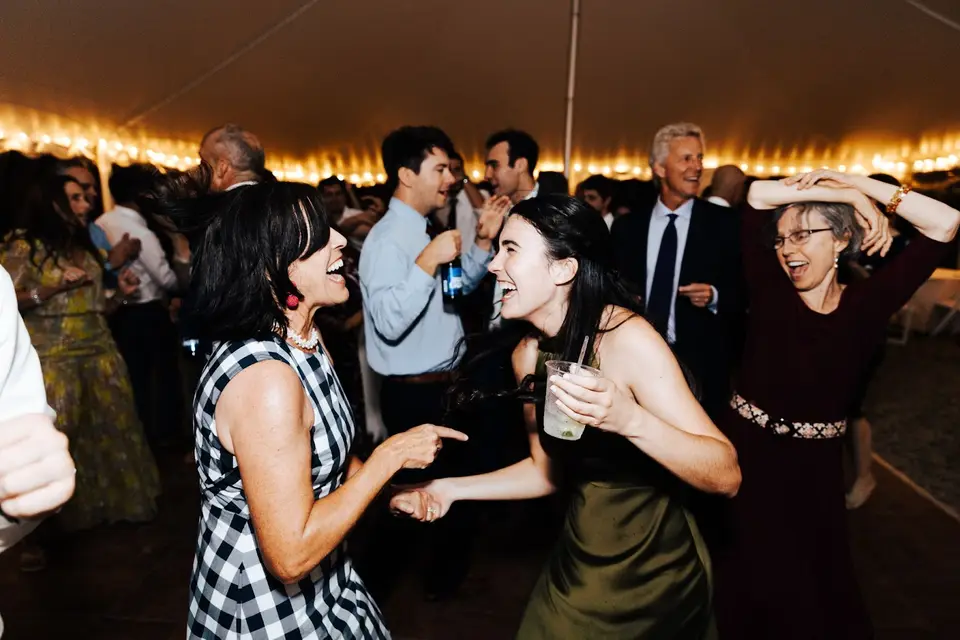 Guests laughing and dancing at a tent reception with string lights overhead