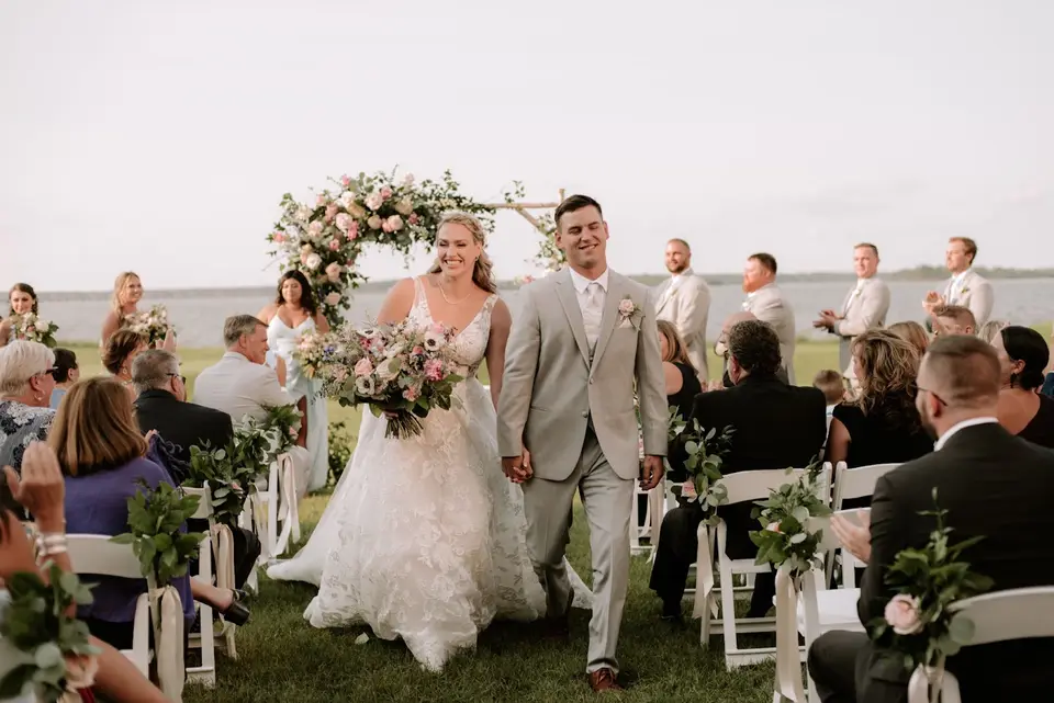 Bride holding a bouquet and groom in a gray suit walking up the aisle past seated guests after their ceremony