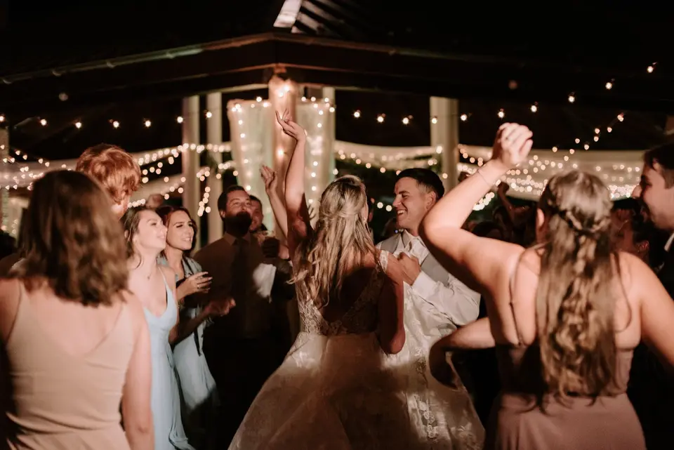 Bride dancing with guests under string lights in an open-air pavilion at night