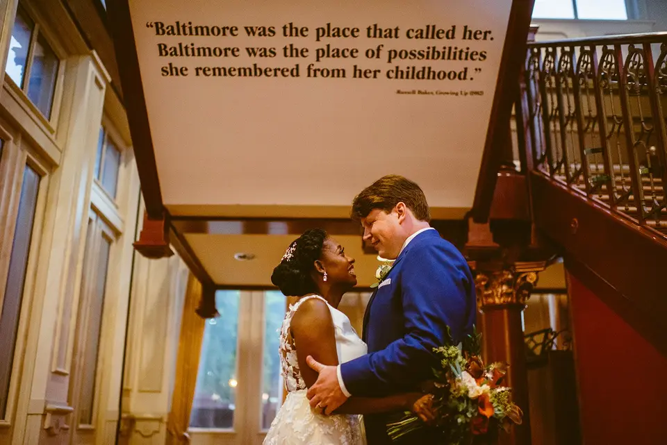 Couple embracing under a wall quote reading Baltimore was the place that called her, inside a historic building