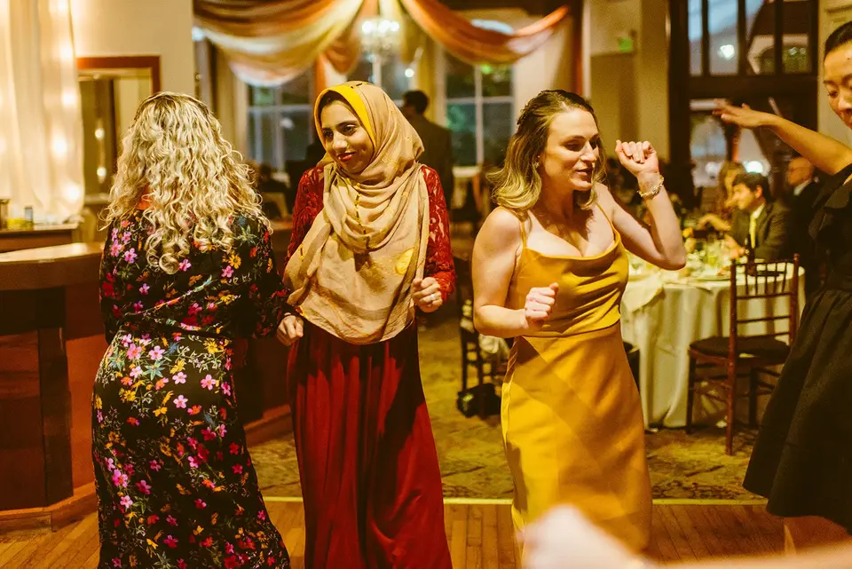 Women in colorful dresses dancing at a wedding reception in a warmly lit ballroom