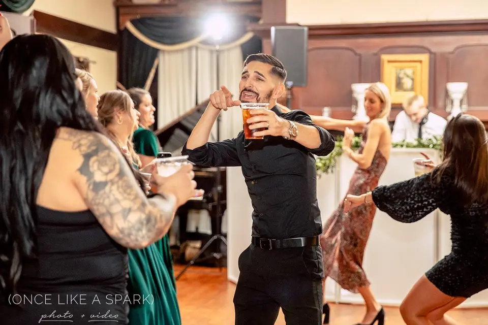 Man in a black shirt holding a beer and dancing with guests at the reception