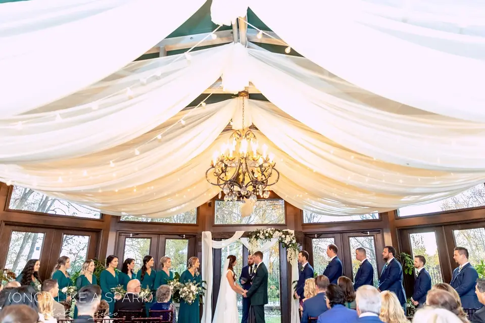 Wedding ceremony under a draped white fabric ceiling with bridesmaids in teal and a chandelier