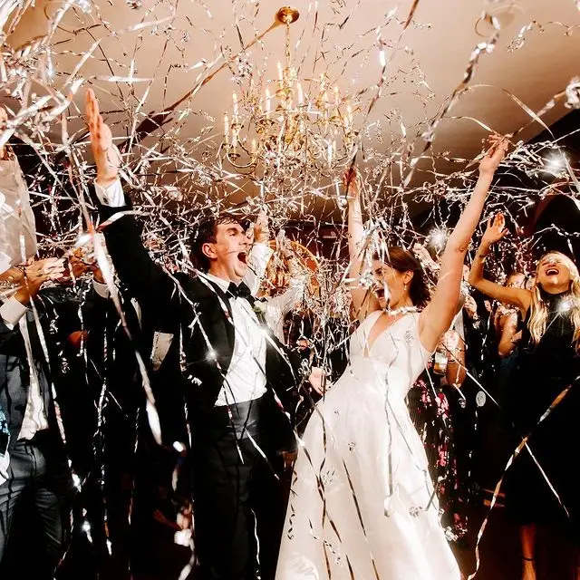 Bride and groom cheering with arms raised as metallic streamers fall around them on the dance floor